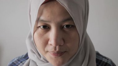 Mutlu Asyalı Müslüman kadın portresi tesettür giymiş kameraya bakıyor ve gülümsüyor, güler yüzlü, arkadaş canlısı bir ifade.