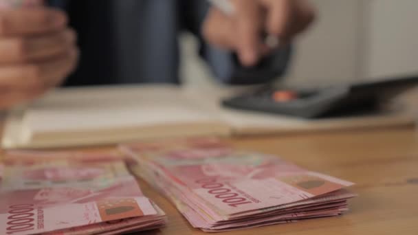Gros plan de la main de la femme comptant l'argent uang roupie indonésienne et prendre des notes, concept de gestion financière de l'argent — Video