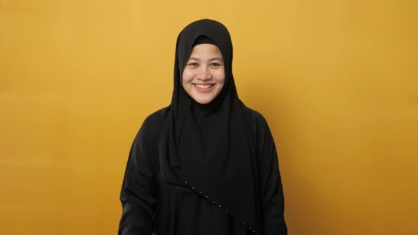 穆斯林妇女的画像 头戴头巾 看着摄像机笑着挥挥手 在黄色背景下打招呼或告别 — 图库视频影像