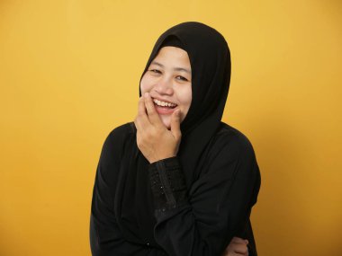 Sarı arka planda komik, neşeli bir ifade görmek için tesettürlü Müslüman kadının portresi.