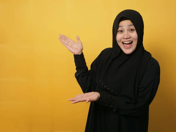 幸せアジアのイスラム教徒の女性は笑顔と彼女の側に何かを提示することを指す コピースペースと黄色の背景に — ストック写真