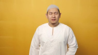 Genç Müslüman Asyalı adamın portresi sarı arka planda karın ağrısı çektiği için midesini sıkıyor.