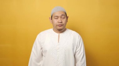 Asyalı genç Müslüman adamın portresi, üzgün yüz ifadesini baş parmakları aşağıda, sarı arka planda gösteriyor.