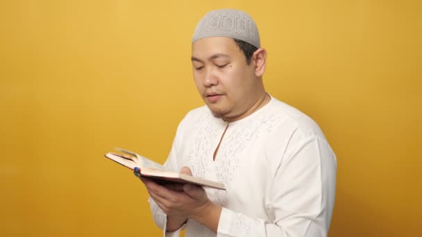 黄色を背景にした聖クルアーンを読む若いアジア系ムスリム男性の肖像 イスラーム的主題 ラマダーン カレーム またはイード ムバラクの概念 — ストック動画