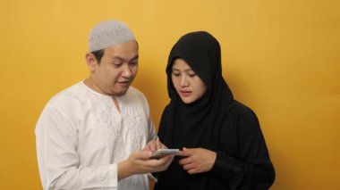 Asyalı Müslüman bir çiftin portresi akıllı telefondan bir şey görünce şaşırdı ya da şok oldu. Mutlu bir yüz ifadesi kazandı.