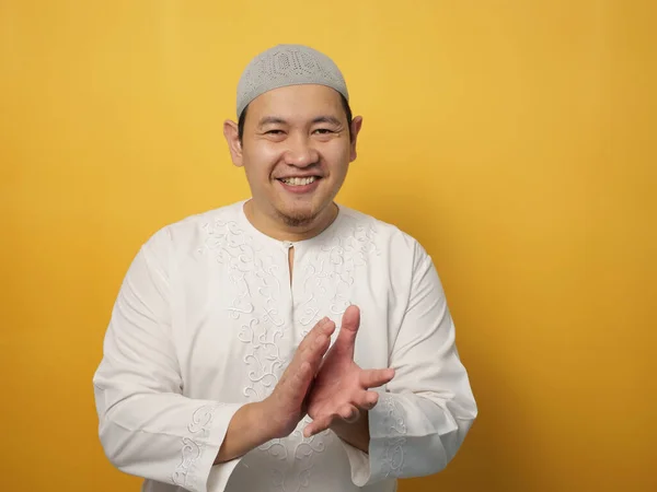 Portrait of happy proud Asian muslim man clapping gesture, half body portrait on yellow background