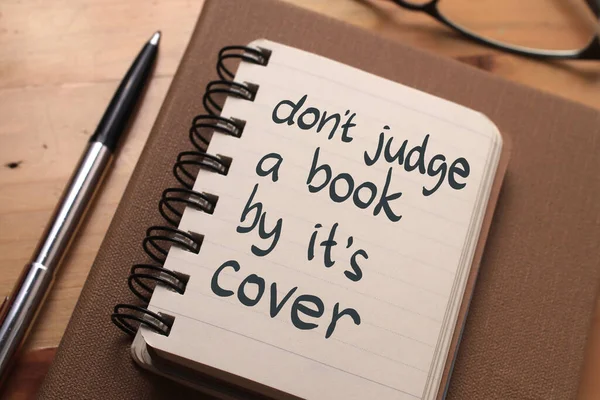 Dont judge a book by its cover, text words typography written on book against wooden background, life and business motivational inspirational concept