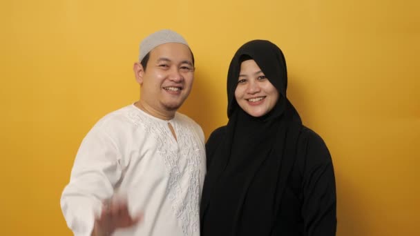 Portré muszlim pár néz kamera mosolygott, és integetett a kezét köszönés vagy búcsú gesztus sárga háttér — Stock videók