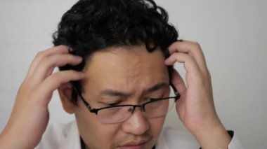 Stresli Asyalı iş adamı kafasını kaşıyor, sorunu için endişeleniyor, yüz ifadesini kapatıyor.