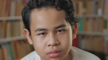 Asyalı bir çocuğun hüzünlü ifadesi, kitap kabuğu kütüphanesi arka planı