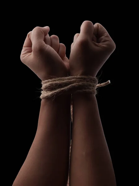 Person hands tied with rope isolated on black dark background, captive victim restrained concept