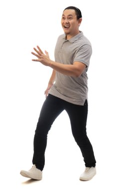 Gri gömlekli, siyah kot ve beyaz ayakkabılı Asyalı bir adam, kendi tarafından şaşırmış, neşeli bir ifade. Tüm vücut portresi izole edildi.