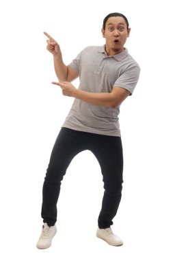 Gri gömlekli, siyah kot ve beyaz ayakkabılı, gülümseyen, işaret eden ya da kendi tarafında bir şey sunan bir adam. Tüm vücut portresi izole edildi.