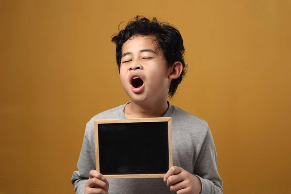 年轻的亚洲学生男孩看起来疲惫而困倦 一边打呵欠 一边拿着空白黑板 在黄色背景下 — 图库照片