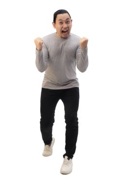Gri gömlekli, siyah kot ve beyaz ayakkabılı bir adam zaferi kutluyor, elini kaldırıyor ve kazanıyor. Tüm vücut portresi izole edildi.
