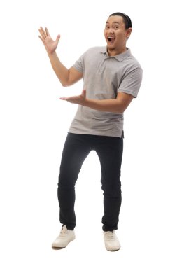 Gri gömlekli, siyah kot ve beyaz ayakkabılı, gülümseyen, işaret eden ya da kendi tarafında bir şey sunan bir adam. Tüm vücut portresi izole edildi.