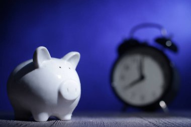 Piggybank ve alarm saati, yatırım parası yönetimi ve zaman ilişkisi kavramı. Mavi ışığın altında