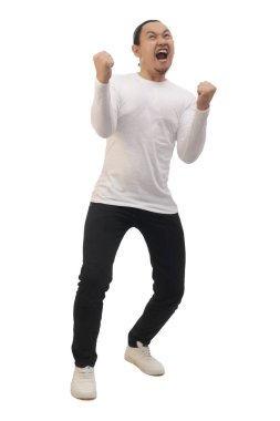 Günlük beyaz gömlekli, siyah kot ve beyaz ayakkabılı bir adam zaferi kutluyor, elini kaldırıyor ve kazanıyor. Tüm vücut portresi izole edildi.