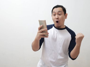 Mutlu, heyecanlı Asyalı genç adam bağırarak gülümsüyor ve akıllı telefonuna bakıp iyi haber konseptini alırken kazanan bir jest gösteriyor.