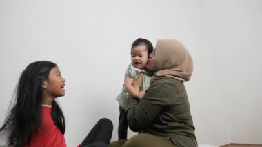 Mutlu Asyalı Müslüman anne yerde oturuyor ve iki kızıyla bağ kuruyor.