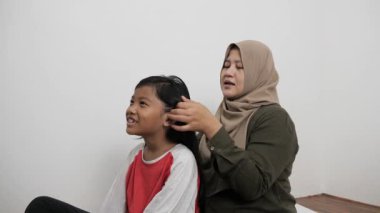 Asyalı Müslüman anne, küçük kızının saçını şekillendiriyor ve bağlıyor. Hikayelerini paylaşıyor. Mutlu aile anları.