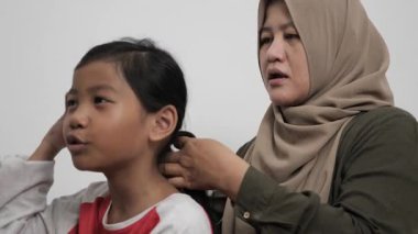 Asyalı Müslüman anne, küçük kızının saçını şekillendiriyor ve bağlıyor. Hikayelerini paylaşıyor. Mutlu aile anları.