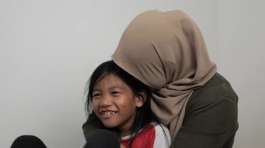 Neşeli Asyalı Müslüman anne ve kızı birlikte gülüyor ve hikayelerini paylaşıyorlar, mutlu aile.