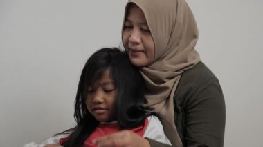 Neşeli Asyalı Müslüman anne ve kızı birlikte gülüyor ve hikayelerini paylaşıyorlar, mutlu aile.