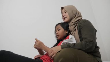 Neşeli Asyalı Müslüman anne ve kızı birlikte gülüyor ve hikayelerini paylaşıyorlar, mutlu aile.