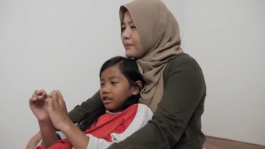 Neşeli Asyalı Müslüman anne ve kızı birlikte gülüyor ve hikayelerini paylaşıyorlar, mutlu aile.