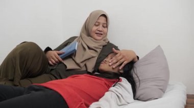 Asyalı Müslüman anne yatağında kızına masal okuyor, mutlu bir aile ilişkisi.