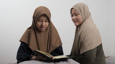 Asyalı Müslüman anne kızına evde Kur 'an okumayı öğretiyor, Arapça yazılar ve Kuran ayetleri öğreniyor.