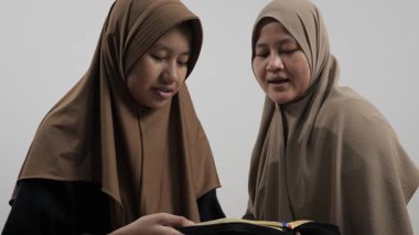 Asyalı Müslüman anne kızına evde Kur 'an okumayı öğretiyor, Arapça yazılar ve Kuran ayetleri öğreniyor.