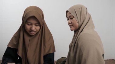 Asyalı Müslüman anne kızına evde Kur 'an okumayı öğretiyor, Arapça yazılar ve Kuran ayetleri öğreniyor.