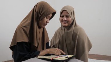 Asyalı Müslüman anne kızına evde Kur 'an okumayı öğretiyor, Arapça yazılar ve Kuran ayetleri öğreniyor.