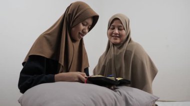 Asyalı Müslüman anne kızına evde Kur 'an okumayı öğretiyor, Arapça yazılar ve Kuran ayetleri öğreniyor.