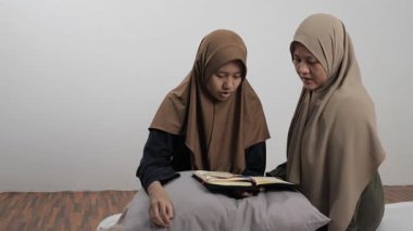 Asyalı Müslüman anne kızına evde Kur 'an okumayı öğretiyor, Arapça yazılar ve Kuran ayetleri öğreniyor.