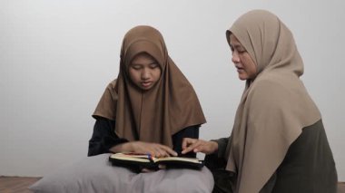 Asyalı Müslüman anne kızına evde Kur 'an okumayı öğretiyor, Arapça yazılar ve Kuran ayetleri öğreniyor.