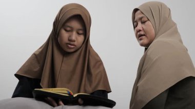 Asyalı Müslüman anne kızına evde Kur 'an okumayı öğretiyor, Arapça yazılar ve Kuran ayetleri öğreniyor.