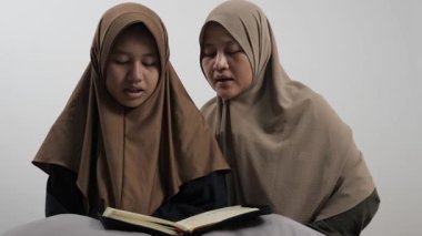 Asyalı Müslüman anne kızına evde Kur 'an okumayı öğretiyor, Arapça yazılar ve Kuran ayetleri öğreniyor.
