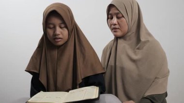 Asyalı Müslüman anne kızına evde Kur 'an okumayı öğretiyor, Arapça yazılar ve Kuran ayetleri öğreniyor.