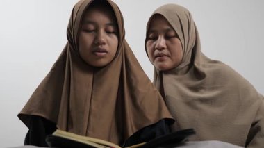 Asyalı Müslüman anne kızına evde Kur 'an okumayı öğretiyor, Arapça yazılar ve Kuran ayetleri öğreniyor.