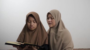 Asyalı Müslüman anne kızına evde Kur 'an okumayı öğretiyor, Arapça yazılar ve Kuran ayetleri öğreniyor.