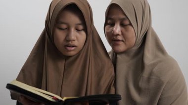 Asyalı Müslüman anne kızına evde Kur 'an okumayı öğretiyor, Arapça yazılar ve Kuran ayetleri öğreniyor.