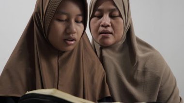 Asyalı Müslüman anne kızına evde Kur 'an okumayı öğretiyor, Arapça yazılar ve Kuran ayetleri öğreniyor.