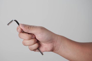 Gri arkaplanda altıgen allen anahtarı tutan bir erkek el.