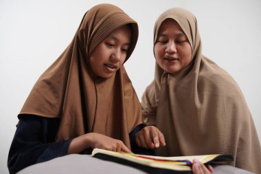 Asyalı Müslüman anne kızına evde Kur 'an okumayı öğretiyor, Arapça yazılar ve Kuran ayetleri öğreniyor.