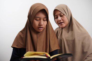 Asyalı Müslüman anne kızına evde Kur 'an okumayı öğretiyor, Arapça yazılar ve Kuran ayetleri öğreniyor.