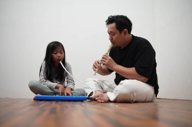 Asyalı bir baba, küçük kızına evde melodi ve kaydedici çalmayı öğreterek, çocuğa müzik aleti tanıtıyor.