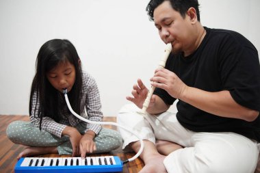 Asyalı bir baba, küçük kızına evde melodi ve kaydedici çalmayı öğreterek, çocuğa müzik aleti tanıtıyor.